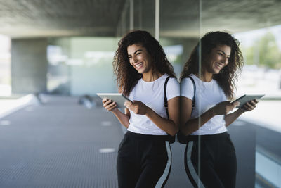 Smiling young woman holding digital tablet while standing by window