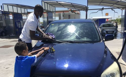 Father son adult child gas station car wash working  cleaning  polishing their dark blue car