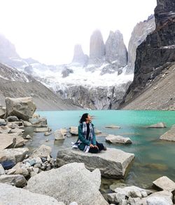 Man sitting on rocks by lake against mountains