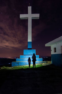 Rear view of silhouette people on cross against sky at night