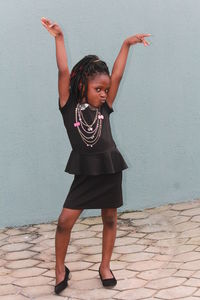 Full length of a girl standing on footpath against wall