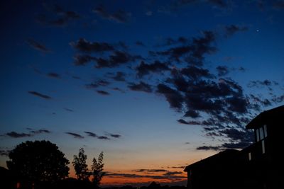 Low angle view of silhouette trees and buildings against sky