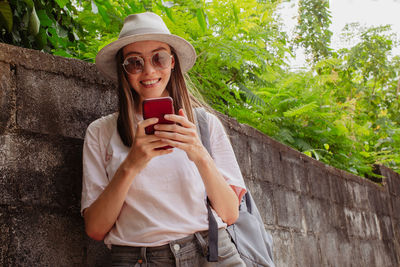 Young woman drinking coffee while standing against plants