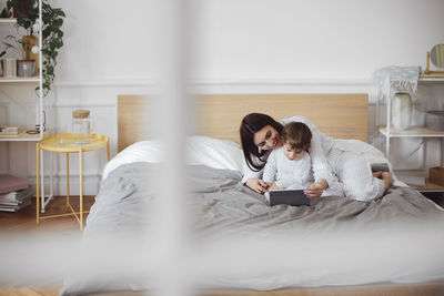 Happy mother using tablet computer with baby boy on bed at home