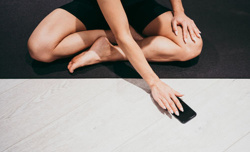 Low section of young woman sitting on mat while using mobile phone at gym