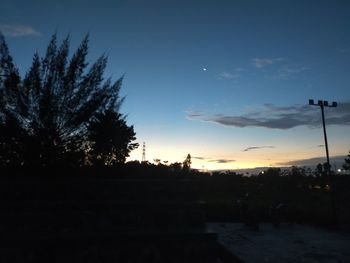 Silhouette trees by street against sky during sunset