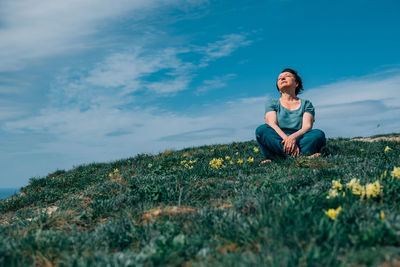 An adult woman, pensioner sits on the grass, legs crossed in a lotus position barefoot with a smile