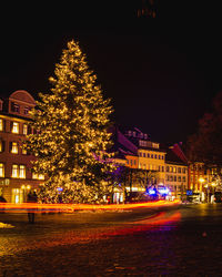 Illuminated christmas tree by building against sky at night