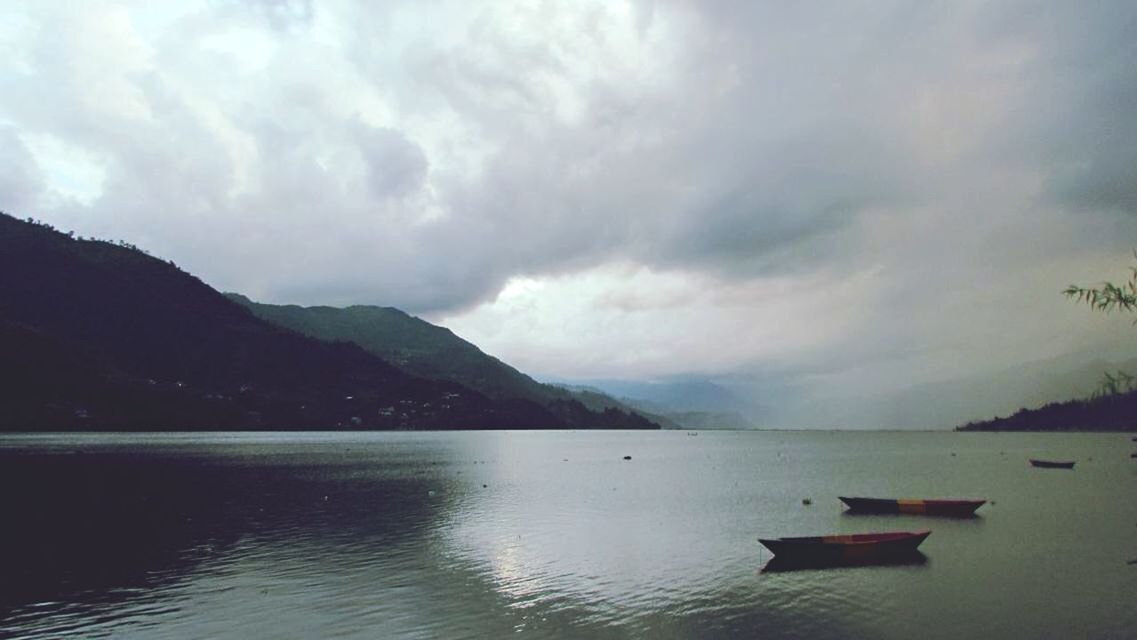 water, mountain, sky, cloud - sky, tranquility, tranquil scene, cloudy, scenics, lake, beauty in nature, mountain range, nature, weather, waterfront, overcast, nautical vessel, cloud, idyllic, boat, sea