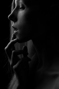 Close-up of young woman touching lips against black background
