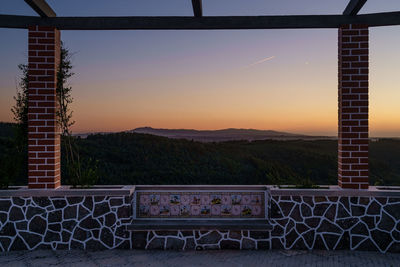 Empty chairs by railing against sky during sunset