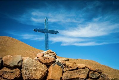 Low angle view of blue cross on rocks against sky