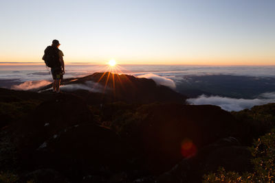 Rear view of man standing on rock against sky during sunset