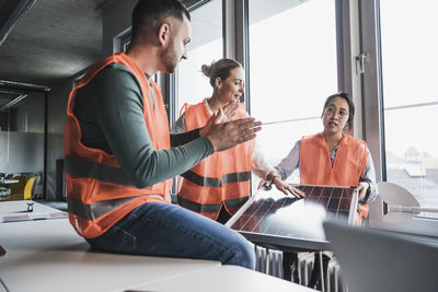 Multiracial colleagues wearing reflective clothing discussing over solar panel at office