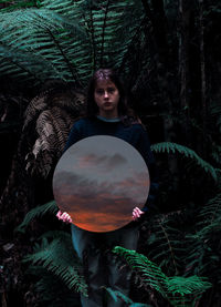 Portrait of woman standing by tree in forest