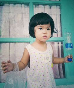 Girl holding plastic bottle while standing by window