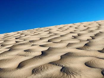 Low angle view of sand dunes against clear blue sky