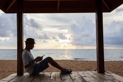 Man sitting by sea against sky