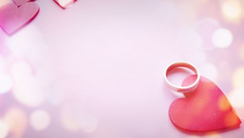 Close-up of wedding ring with red heart shapes over pink background