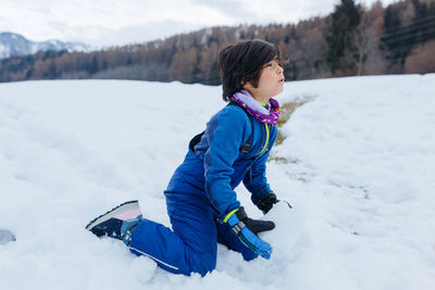 Sitting on the snow girl in blue winter clothes and making snow ball on the hill making snowman