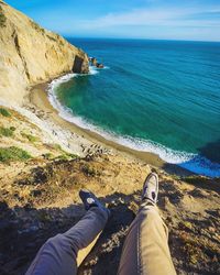 Low section of person sitting on mountain against sea