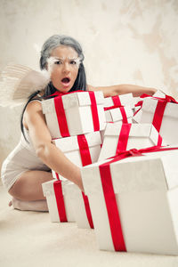 Portrait of angry female model in angel costume holding christmas presents