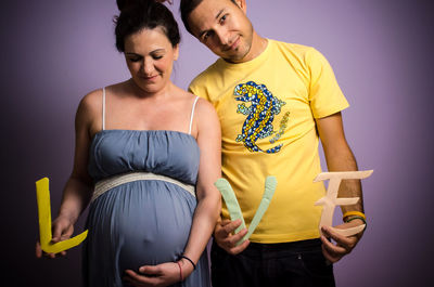 Portrait of smiling man with pregnant woman holding love alphabets