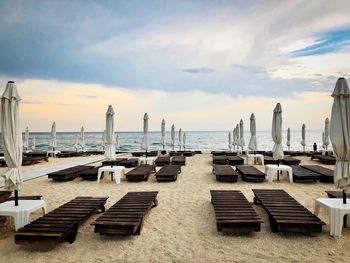 A beach with empty wooden sunbeds and wooden umbrellas on a day with dark storm clouds