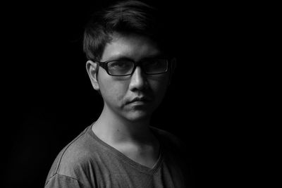 Close-up portrait of young man wearing eyeglasses against black background