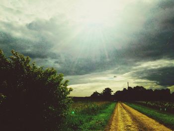 Road passing through field against cloudy sky