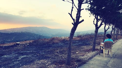 Rear view of man sitting on landscape against sky