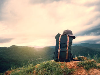 Backpack with cap on cliff against sky