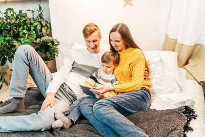 High angle view of cheerful family looking at digital tablet on bed
