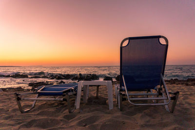 Chair on beach against clear sky during sunset