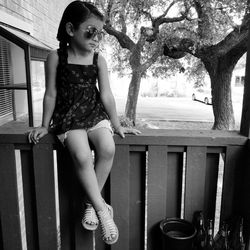 Girl looking away while sitting on railing against trees