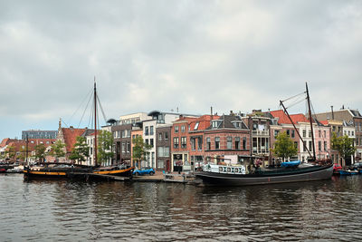 Sailboats moored on river by buildings against sky