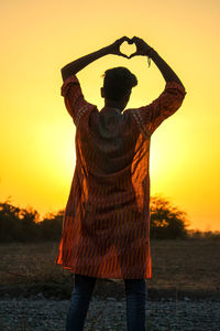 Rear view of man standing against orange sky