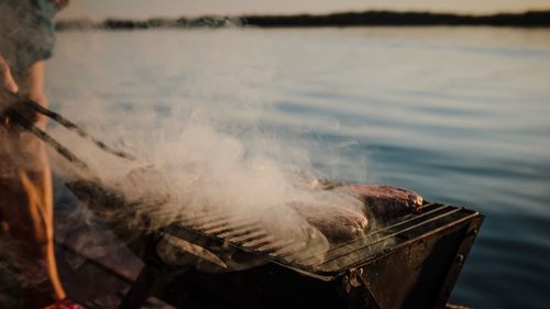 Close-up of meat cooking on barbecue grill by lake
