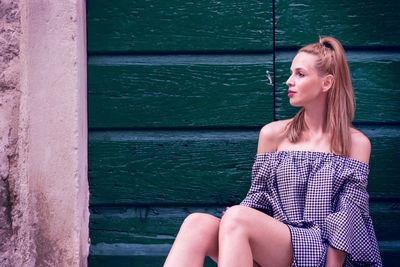 Beautiful young woman sitting against wall