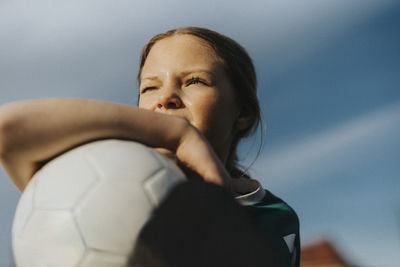 Contemplative elementary girl with sports ball looking away against sky