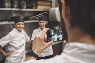 Male chef taking photograph of female coworkers in commercial kitchen