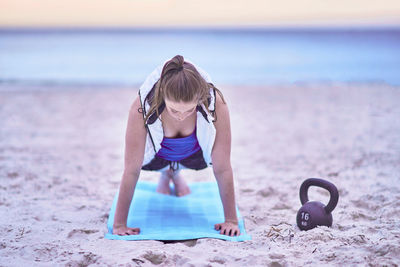 Young woman exercising on exercise mat at beach