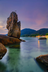 Rock formation in sea against sky during sunset