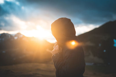 Side view of traveler in jacket with hoodie enjoying landscape of mountain in sunlight
