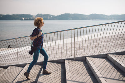 Full length side view of woman climbing steps with sea in background