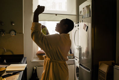 Carefree young woman holding grapes dancing in kitchen at home