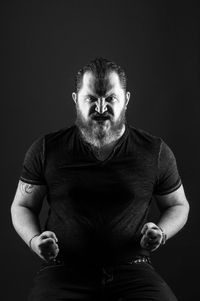 Portrait of angry mid adult man gesturing while sitting against black background