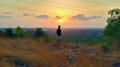 Rear view of man standing on field against sky during sunset