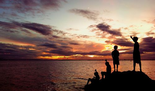 Silhouette of children against sea and moody sky at sunset