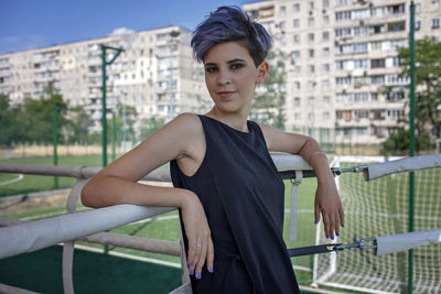 Portrait of young woman standing against railing